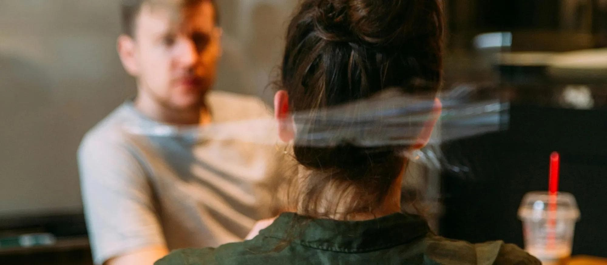 Two people in conversation across a table in a softly lit room, one facing the camera
